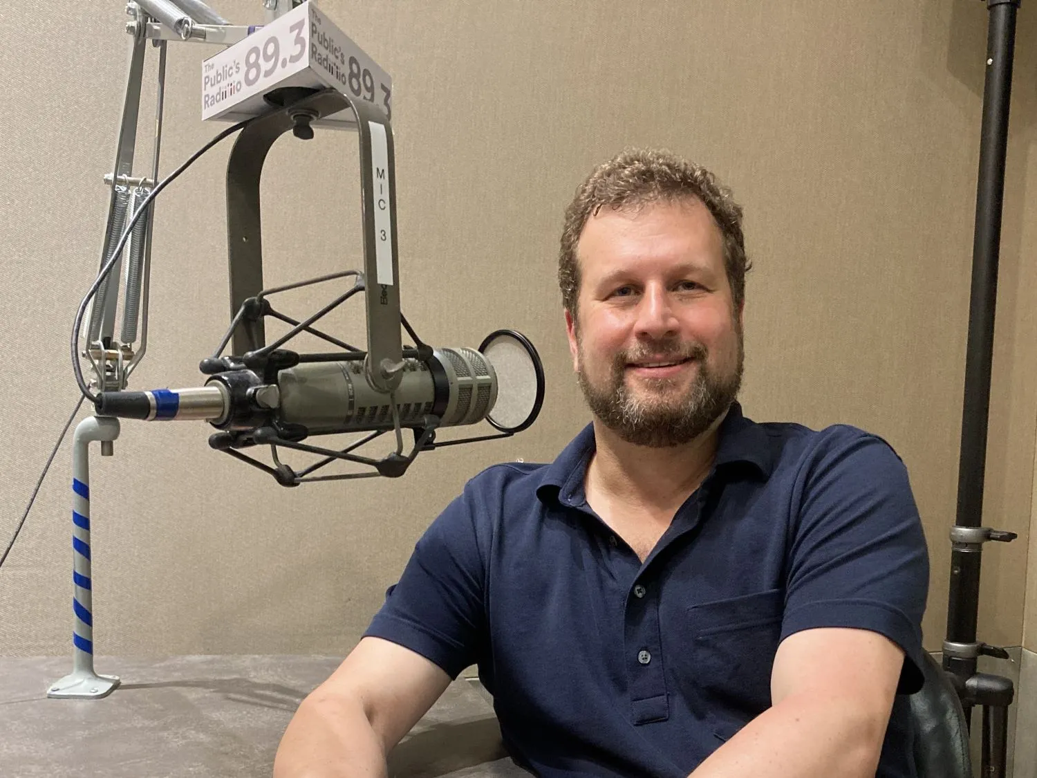 Corey Brettschneider, smiling, seated at a radio studio microphone.